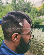 Man with afro textured locs, wearing silver loc jewelry, glasses, and blue top outdoors