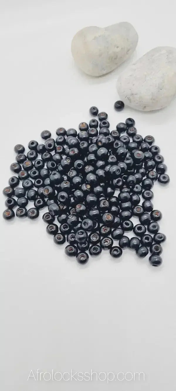 Pile of small black wooden beads for hair or loc accessories on white background with stones