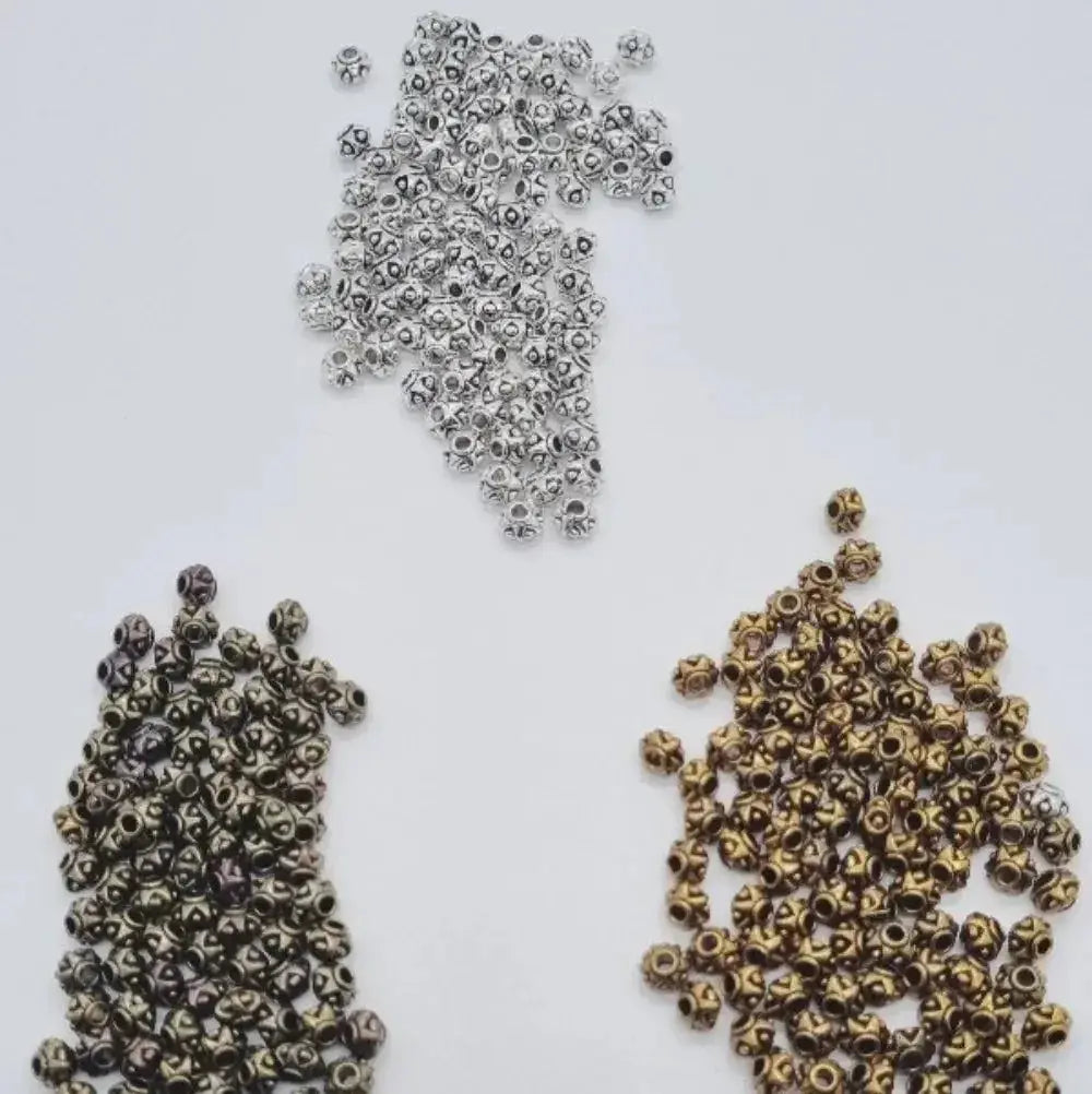 Three piles of 6mm zinc beads in silver, bronze, and gold for braids and microlocks on white background