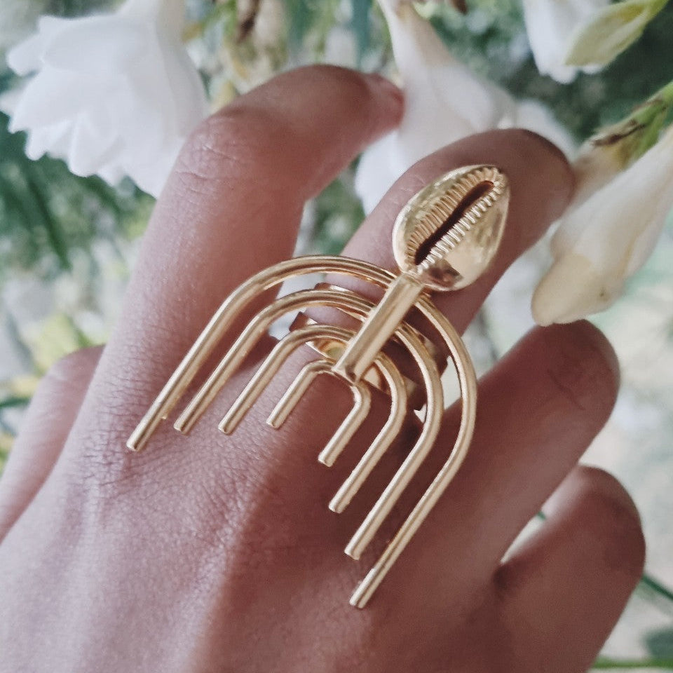 bague metal dore design modern et cauris vu porte sur une main