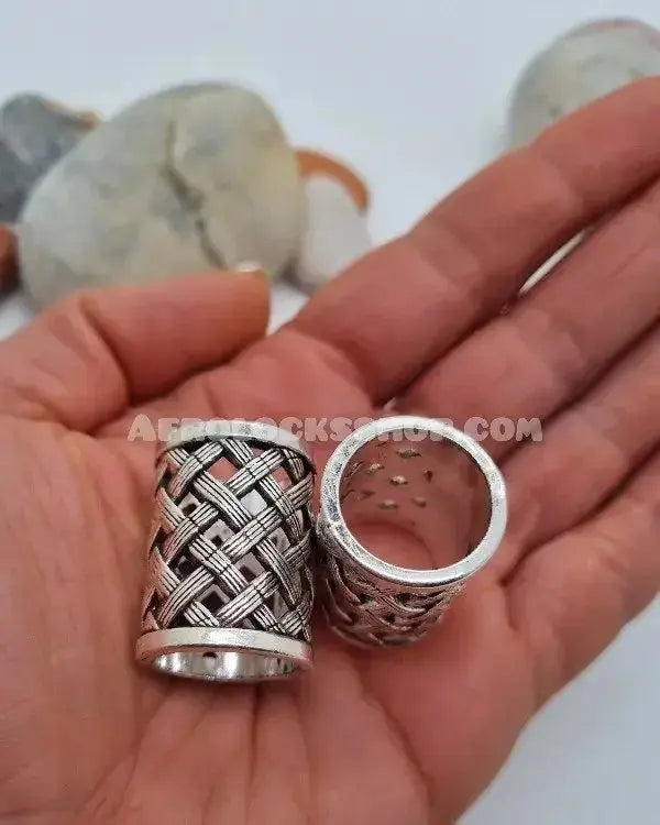 Hand holding two large silver hair beads with woven pattern for braids or locs