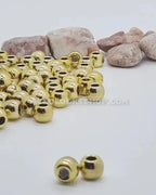Gold hair beads for locks or braids on white surface with natural stones in background