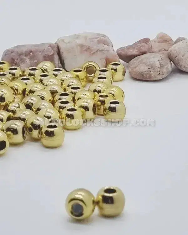 Gold hair beads for locks or braids on white surface with natural stones in background