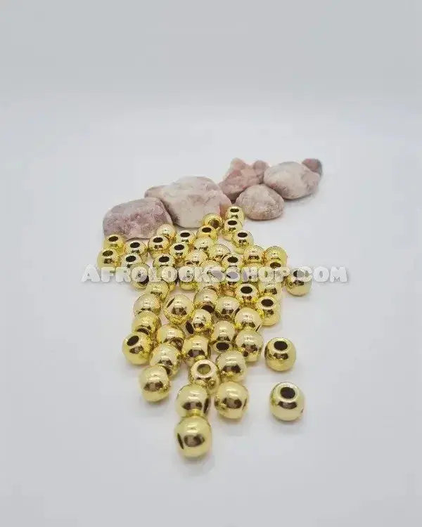 Gold hair beads for locks or braids arranged on a white background with stones behind.